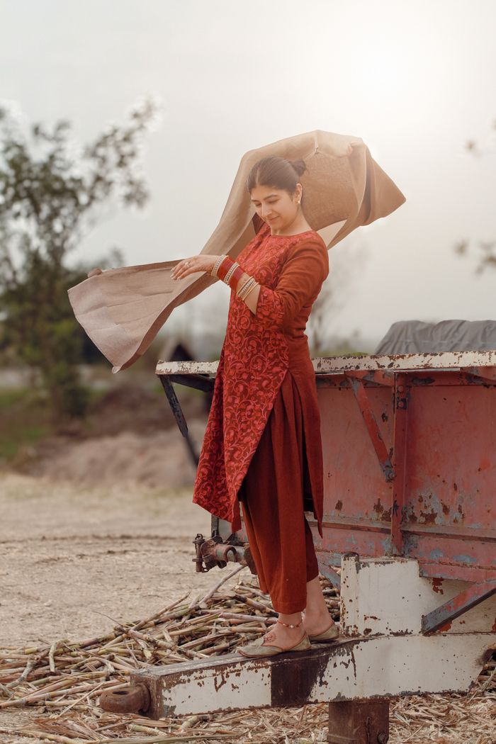 A woman in a red Indian traditional dress poses outdoors in Punjab, India.